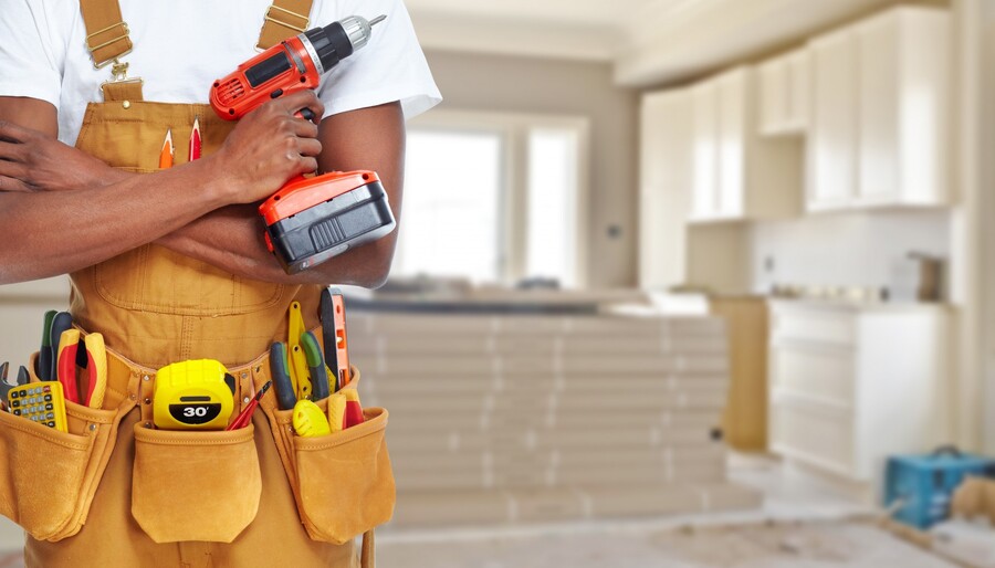 Handyman holding a cordless drill in a kitchen under renovation with tools in a utility belt